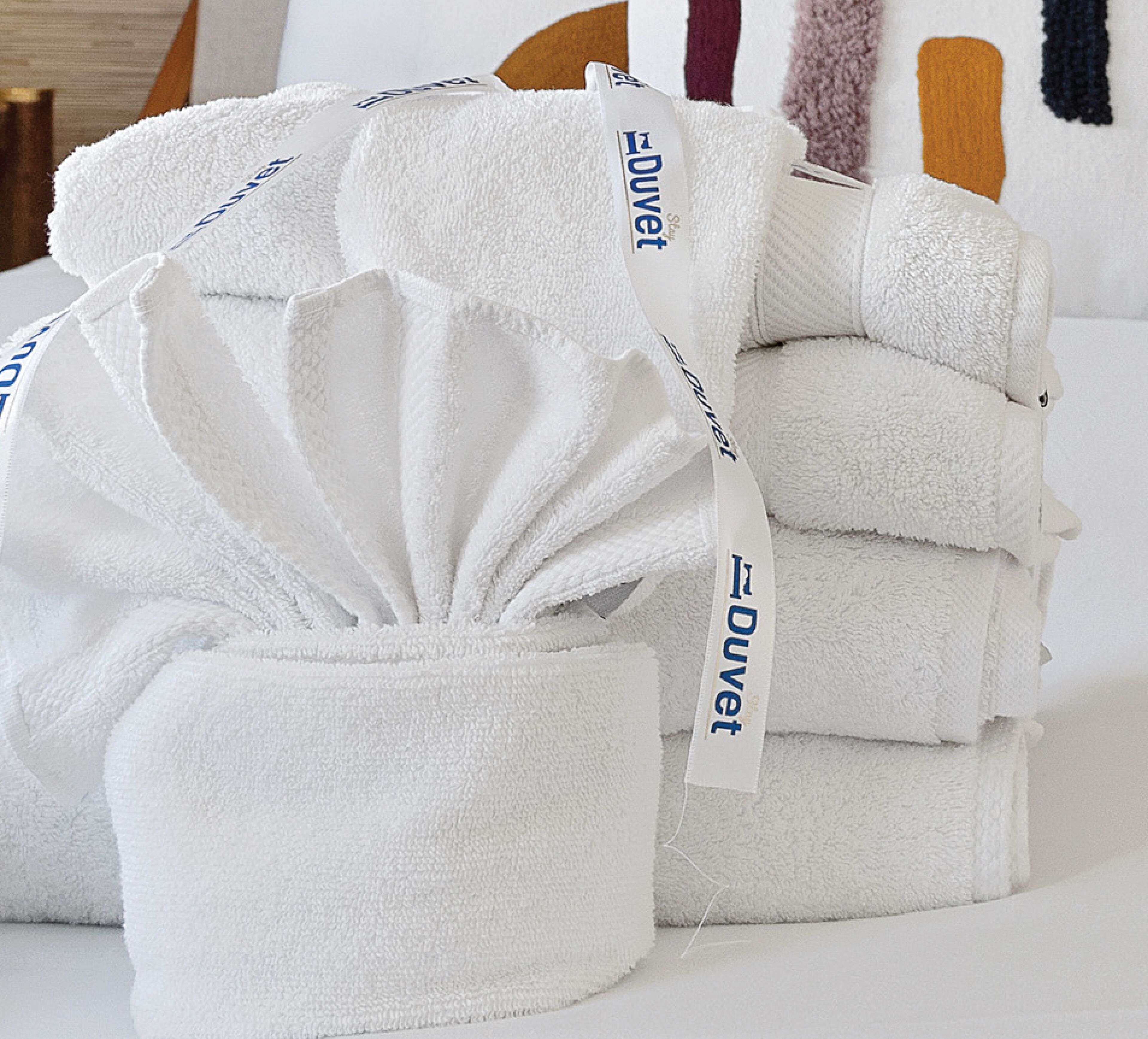A stack of white towels with 'Duvet' tags, neatly arranged on a bed.