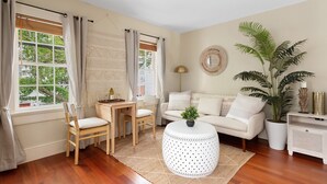 Un salón con piso de madera, una mesa de centro redonda y blanca, un sofá blanco, una mesa de comedor con sillas y una planta grande en maceta.