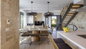 A modern kitchen with a stone wall, a dining area with a table and chairs, and a staircase leading to an upper level. - Perfect Hideaway for Families & Unmatched Sunsets (Rethymno)