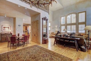 A spacious living room with a dining area, large windows, and a staircase. - Windwood Breckenridge Luxury Mountain Home (Breckenridge)