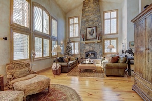 A spacious living room with a fireplace, large windows, and a stone wall. - Amazing Mountain Home! Chefs Kitchen. Excellent Location. Early Checkin. (Breckenridge)