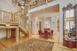 A spacious interior with a wooden staircase, a dining area with chairs, and a large rug on the floor. - Windwood Breckenridge Luxury Mountain Home (Breckenridge)