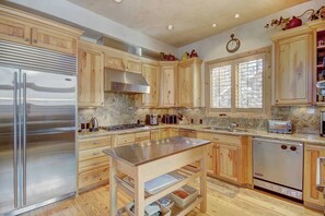 A kitchen with wooden cabinets, stainless steel appliances, a marble countertop, and a window with blinds. - Windwood Breckenridge Luxury Mountain Home (Breckenridge)