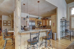 A spacious kitchen with wooden cabinets, a central island with bar stools, and pendant lighting. - Windwood Breckenridge Luxury Mountain Home (Breckenridge)