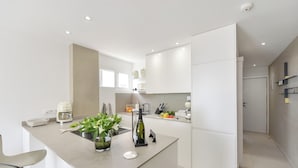 Une cuisine moderne avec des meubles blancs, un îlot central agrémenté d’une plante et un four encastré.