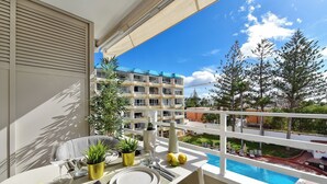Un balcon aménagé avec un coin repas, une piscine et une vue sur un immeuble d’habitation.
