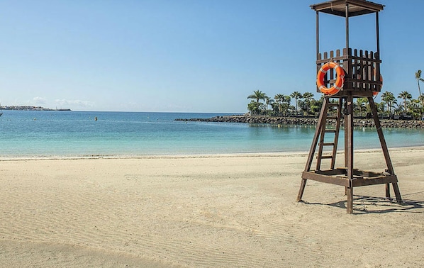 Una torre de salvavidas en una playa con agua azul cristalina y palmeras al fondo.
