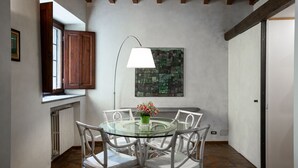 A dining area with a glass table and white wicker chairs, a floor lamp, and a painting on the wall. - Torre dei Sapiti Apartment with private courtyard (Firenze)