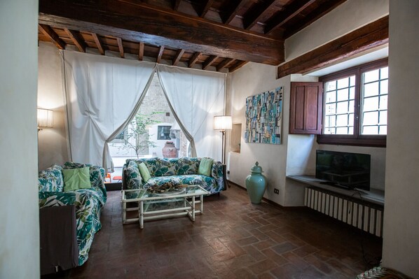 A cozy room with a wooden ceiling, a sofa with a leaf pattern, a glass coffee table, a TV, and a large vase.