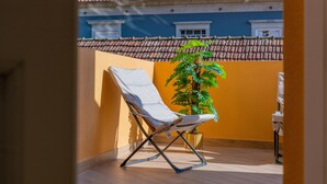 A balcony with a white chair, a potted plant, and a view of a building with a red-tiled roof. - NEW! 75 m2 apartment completely renovated (B) (Guimarães)