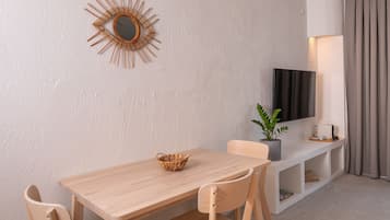 Un salon moderne avec une table en bois, deux chaises, un panier en osier, une plante en pot, un téléviseur à écran plat, une lampe et une grande fenêtre avec des rideaux.