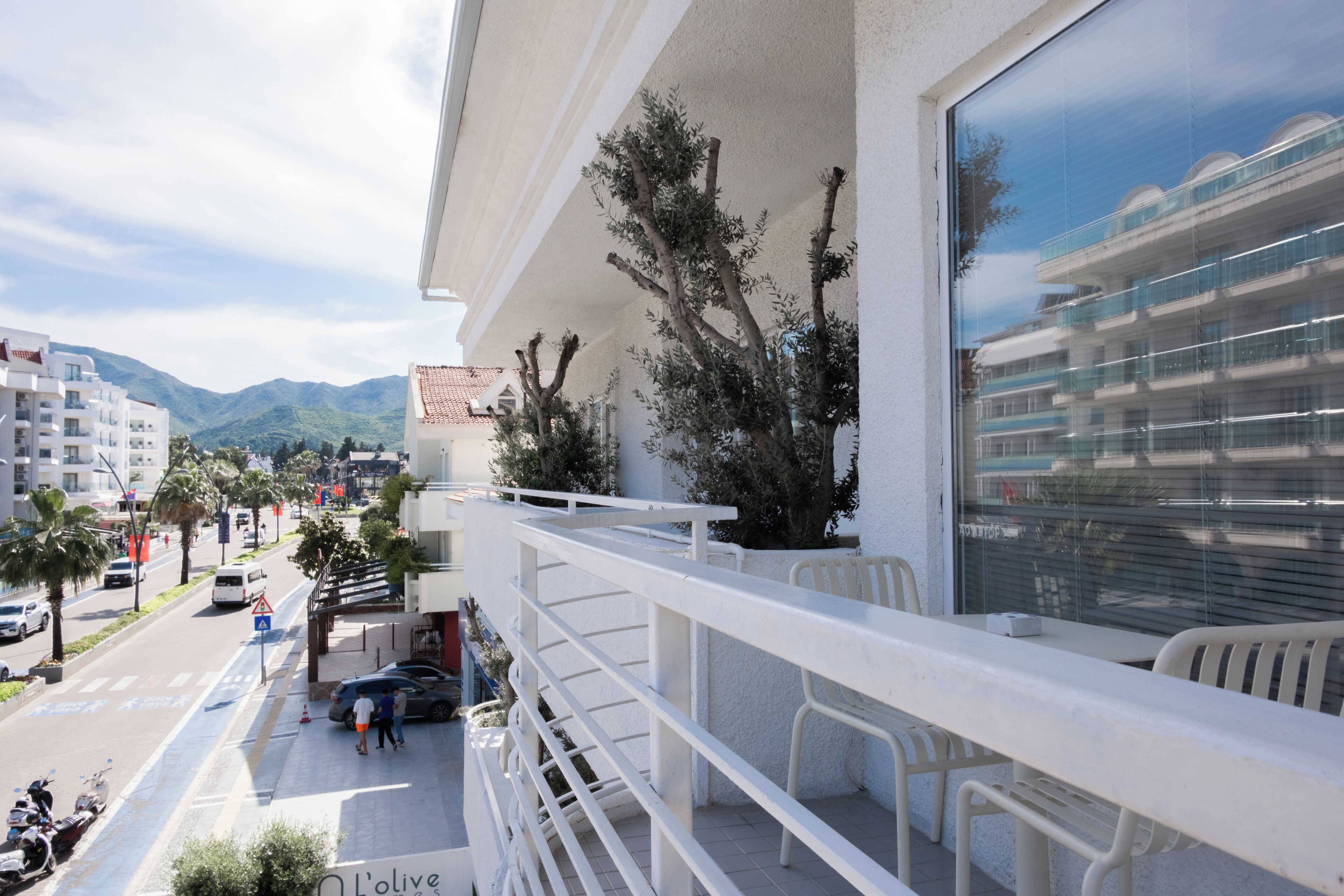 A balcony with a view of a street, a potted plant, and a table with chairs.