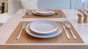 Mesa de comedor preparada con platos, cubiertos y una copa. Se observan apliques decorativos y una pared con textura al fondo.