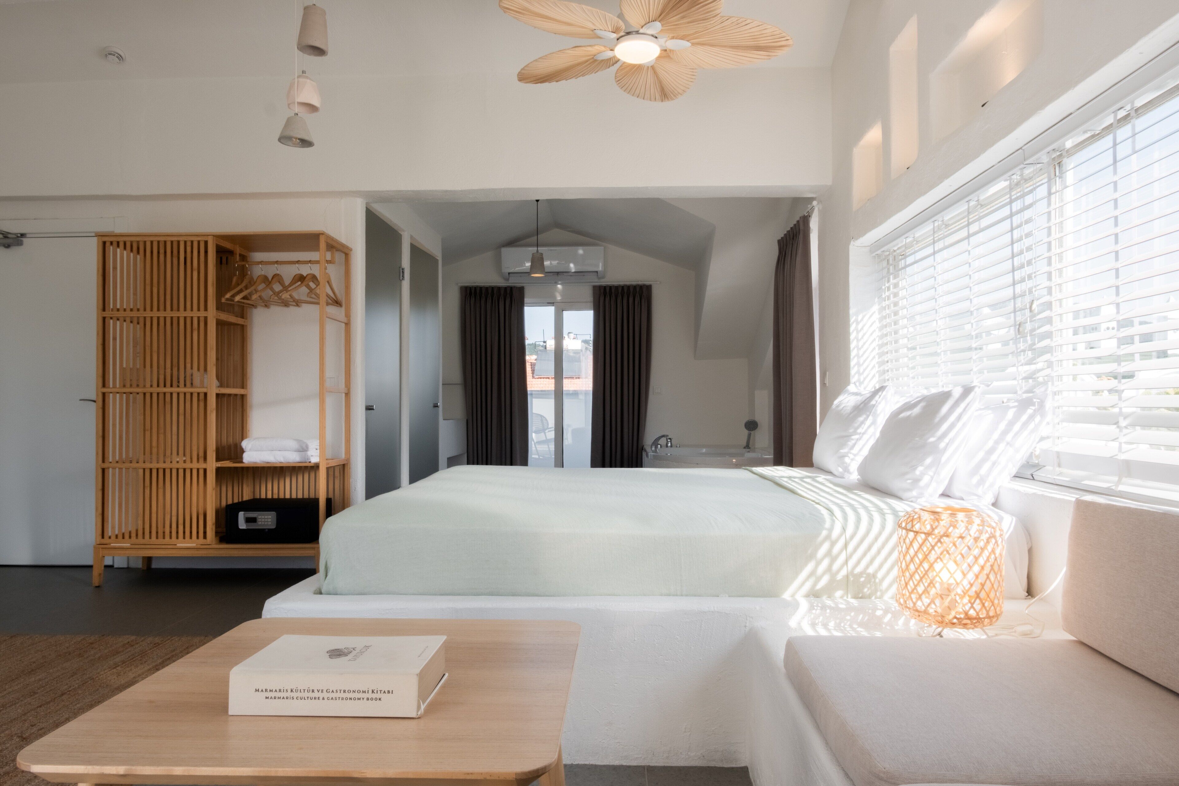 A modern hotel room with a large bed, a wooden wardrobe, a seating area, and a ceiling fan.