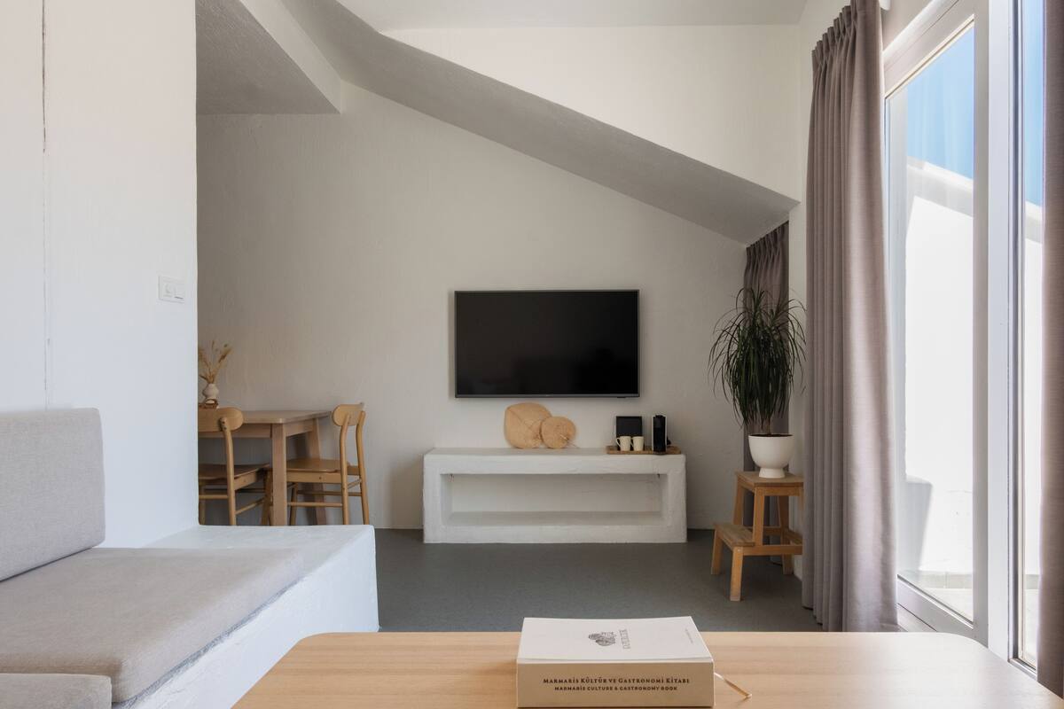Un salon moderne doté d’un téléviseur à écran plat, d’un meuble de rangement blanc, d’une table basse en bois et d’une grande fenêtre agrémentée de rideaux.