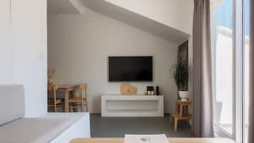 A modern living room with a flat-screen TV, a white entertainment unit, a wooden coffee table, and a large window with curtains.