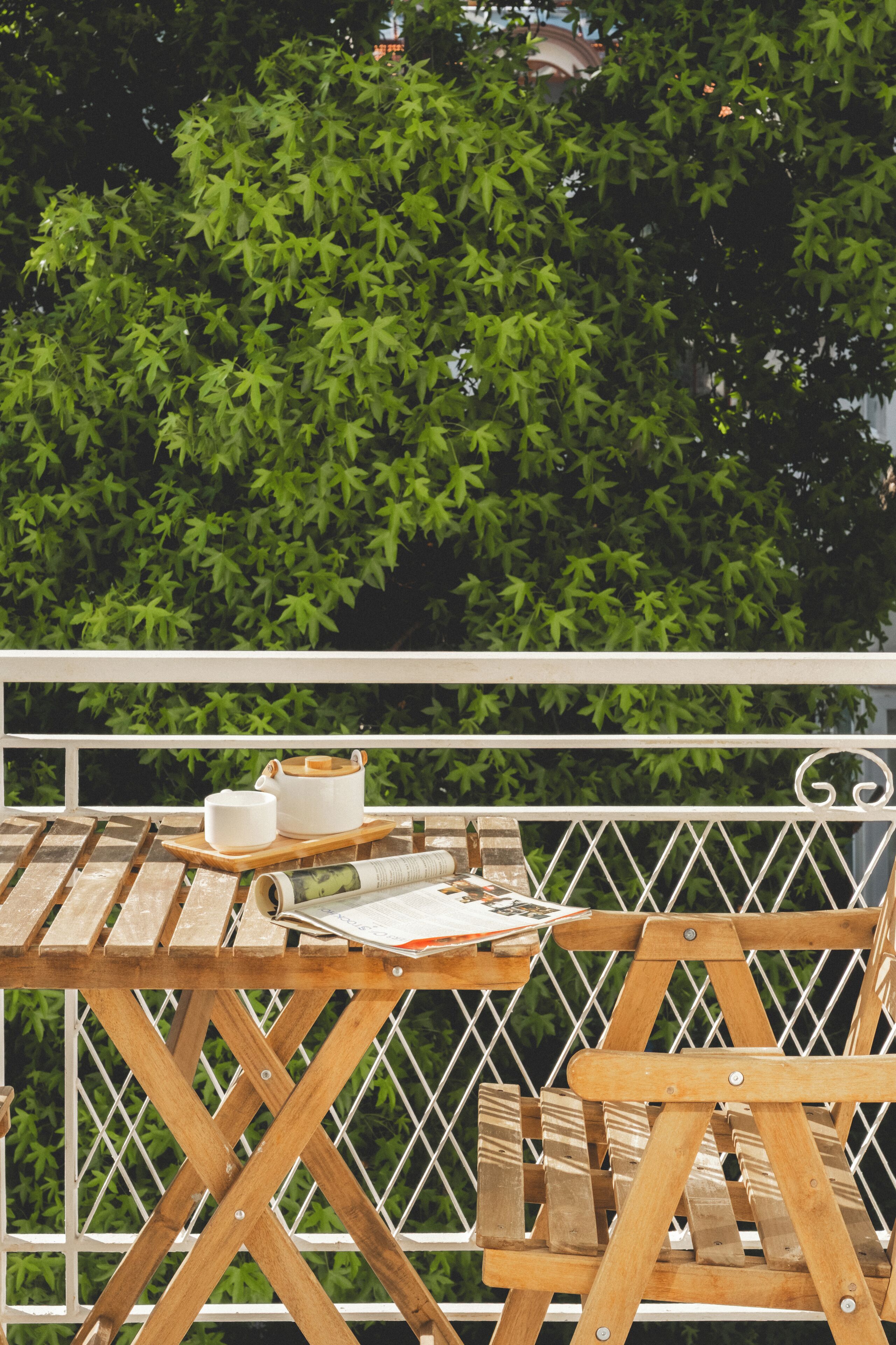 A wooden table with a white pot and a cup, set against a backdrop of green foliage.