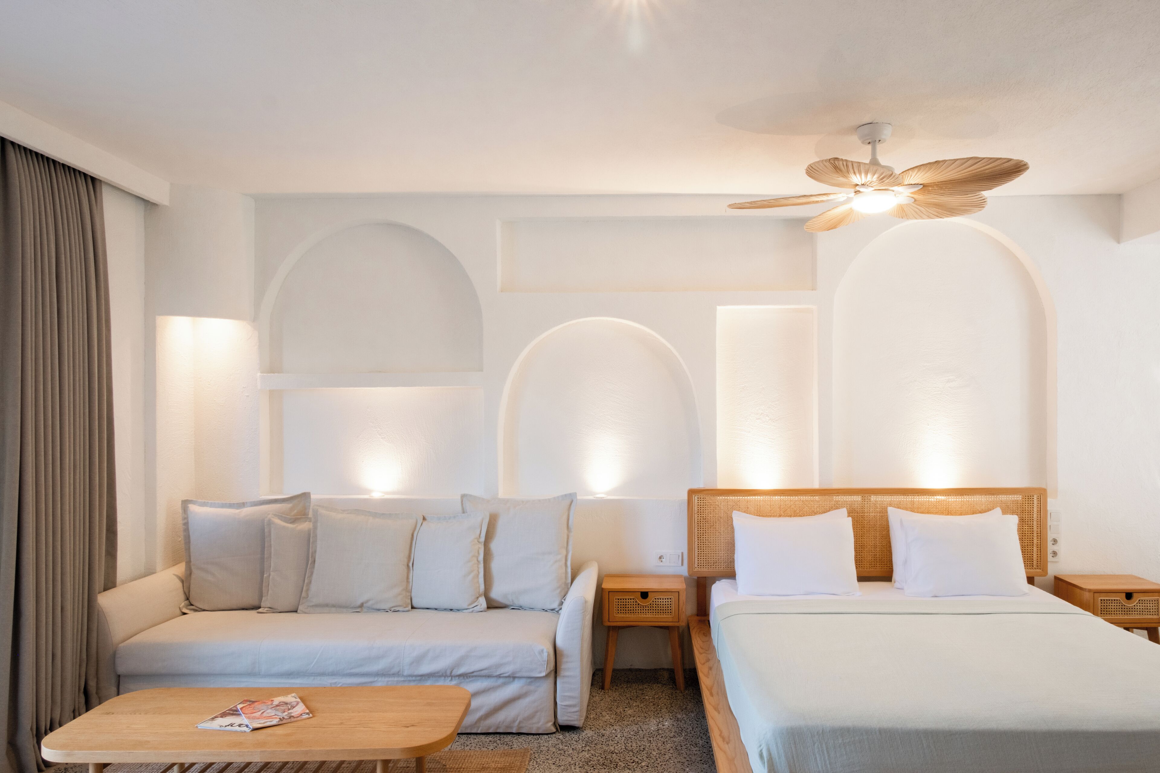 A hotel room with a bed, a sofa, a small table, and a ceiling fan.