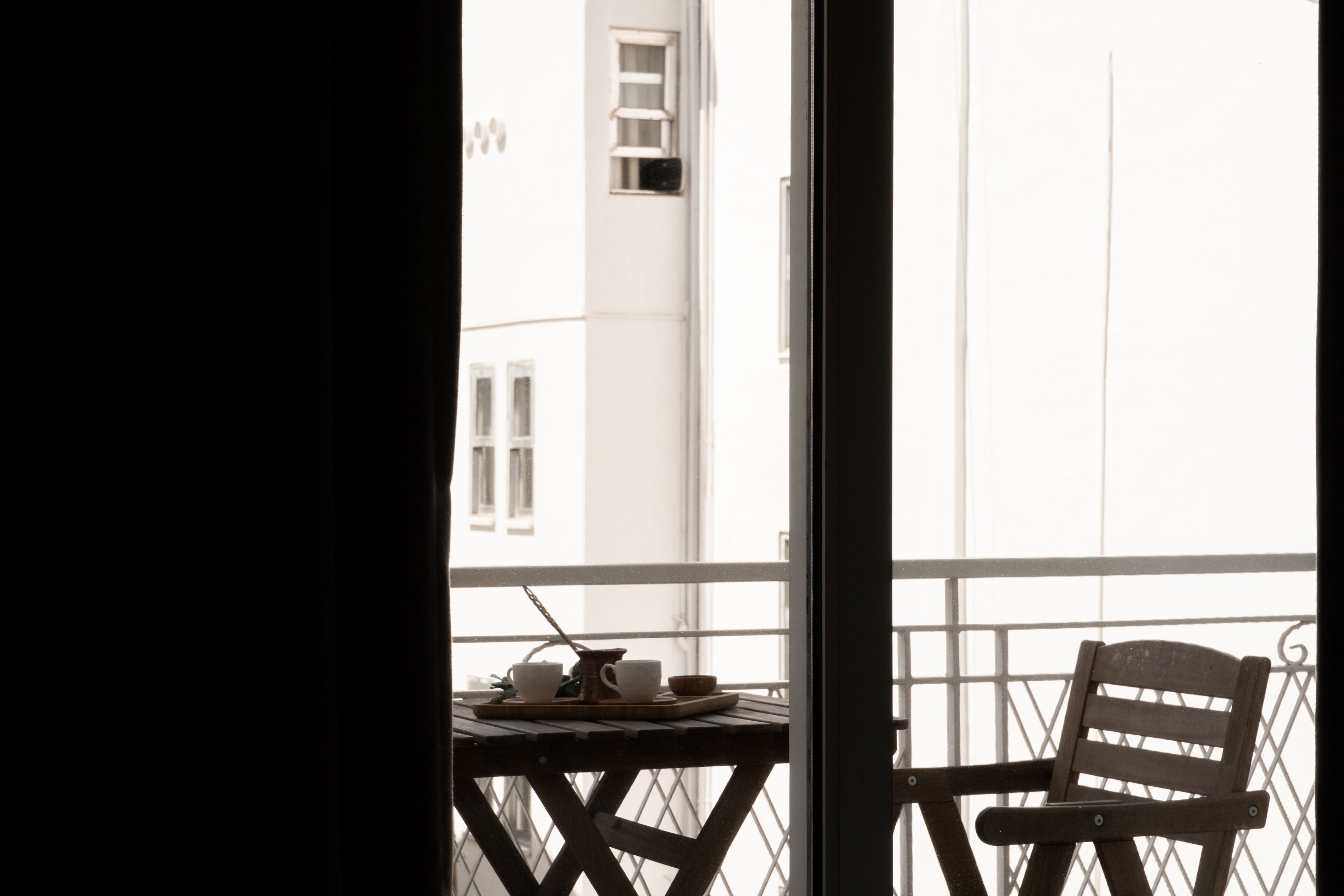 A balcony with a wooden chair and a table with cups and a tray.