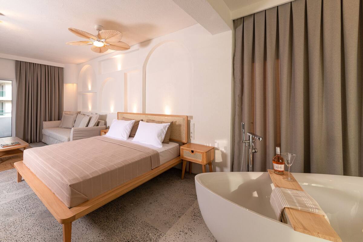 Une chambre d’hôtel moderne dotée d’un grand lit, d’un coin salon, d’une baignoire et d’un balcon avec vue.