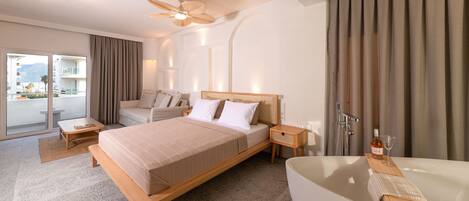 A modern hotel room with a large bed, a sitting area, a bathtub, and a balcony with a view.