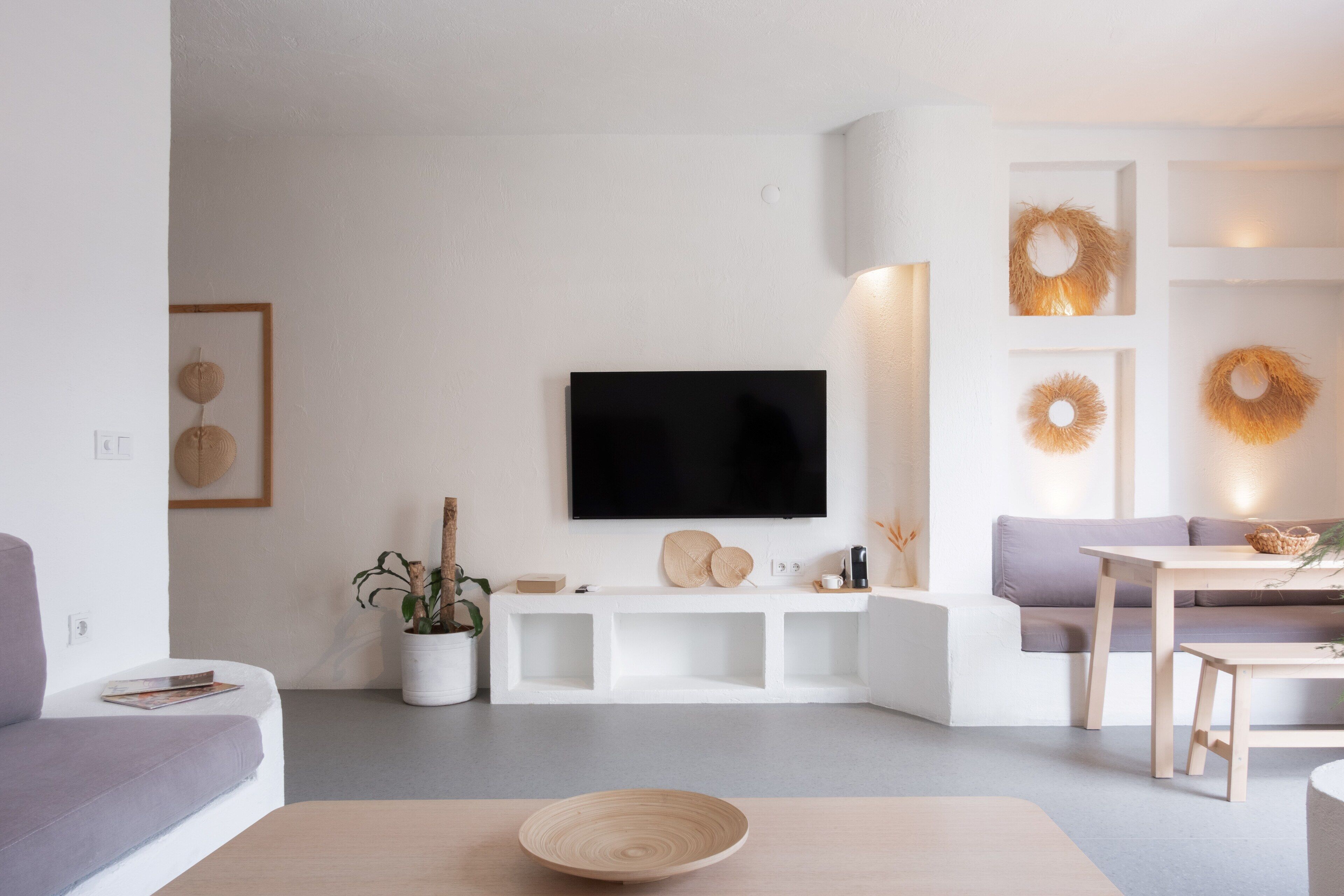 Een moderne woonkamer met een flatscreen televisie aan de muur, een witte salontafel en een grijze bank.
