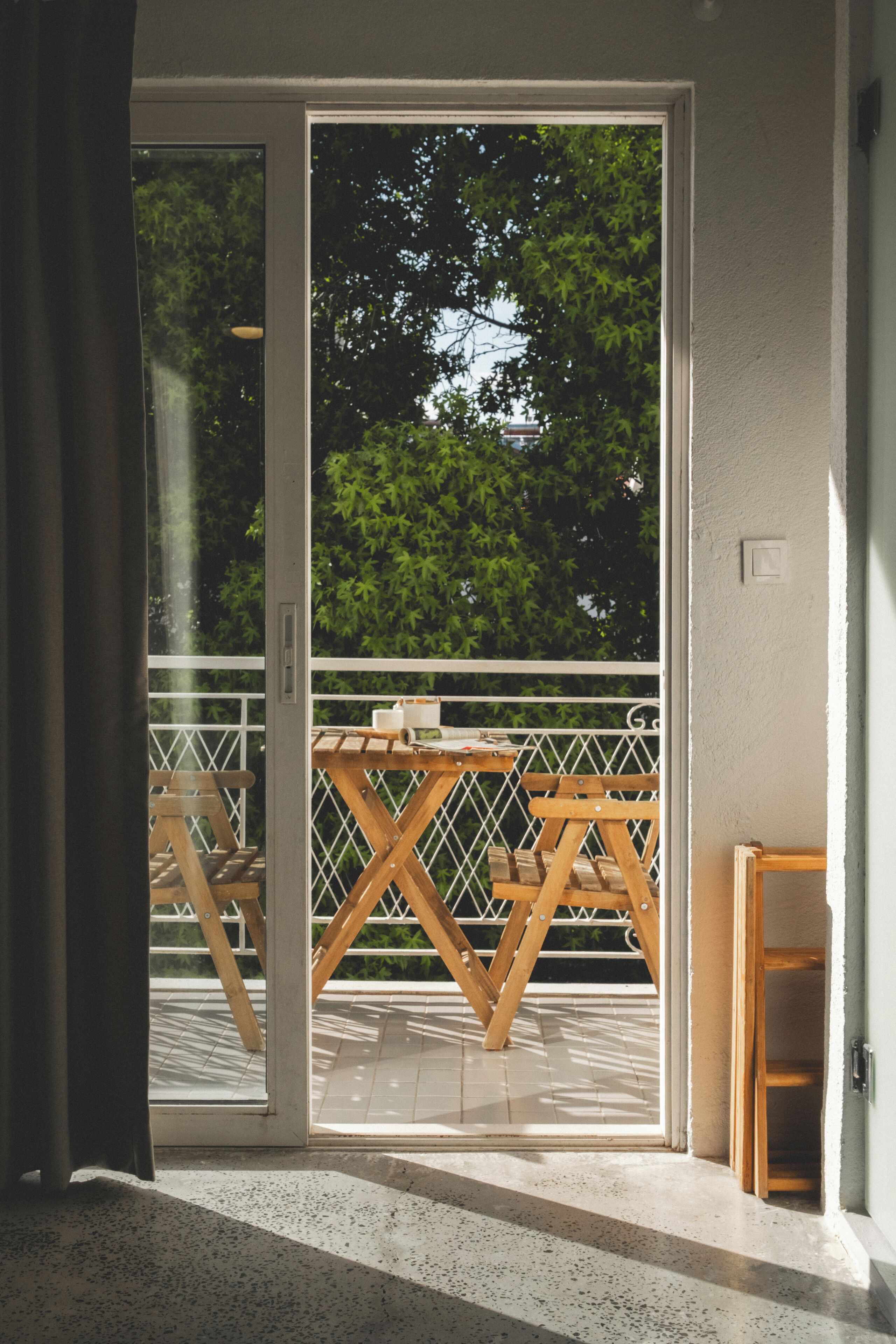 Een kamer met een schuifglasdeur die leidt naar een buitenbalkon met een houten tafel en stoelen.