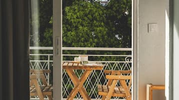 Een kamer met een schuifglasdeur die leidt naar een buitenbalkon met een houten tafel en stoelen.