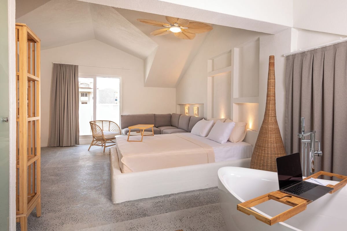 Une chambre à coucher moderne avec un grand lit, une chaise en bois, un bureau et une salle de bain équipée d’une baignoire et d’une douche.