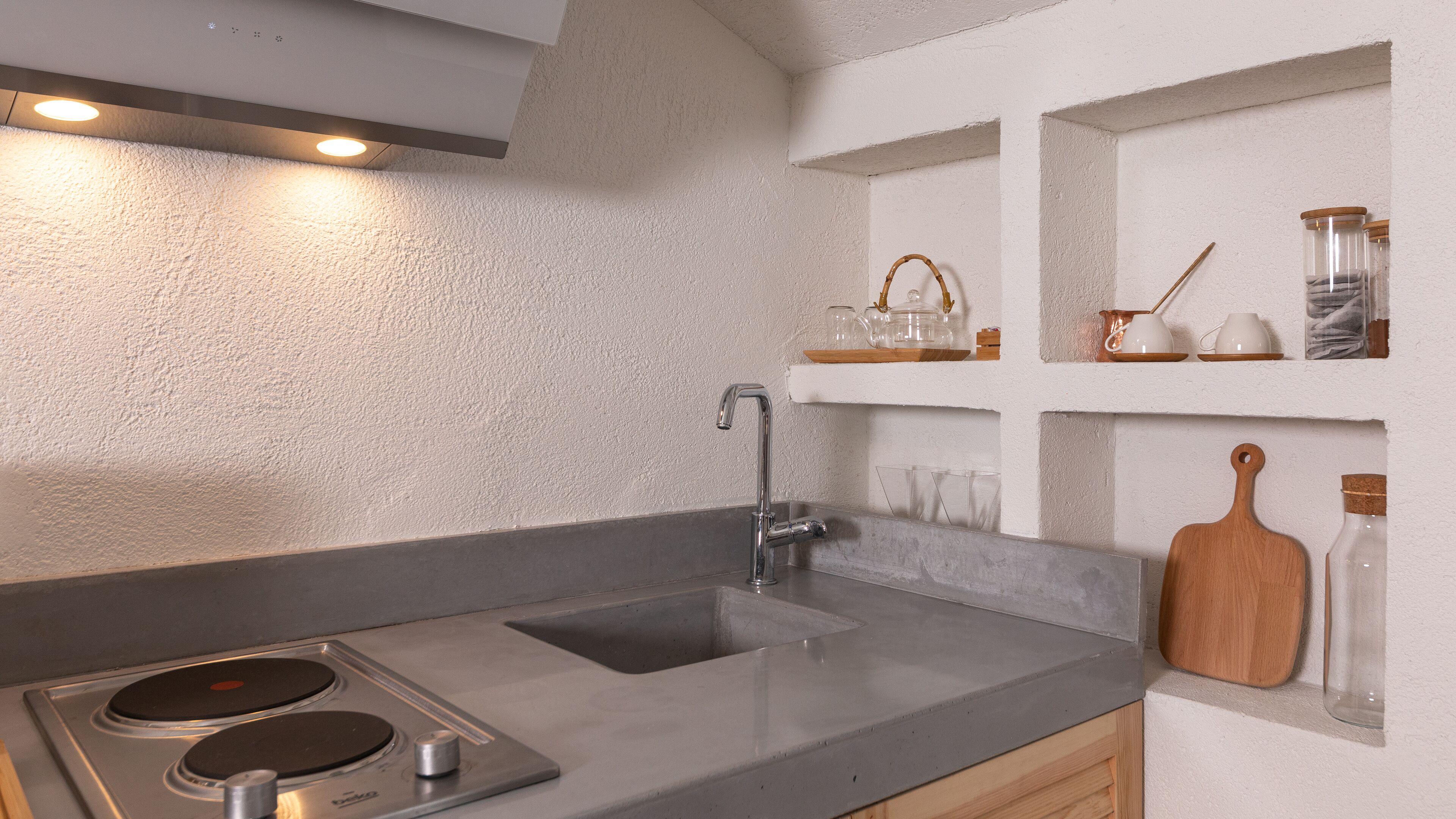 A modern kitchen with a double sink, stainless steel cooktop, and built-in shelves with glassware and jars.