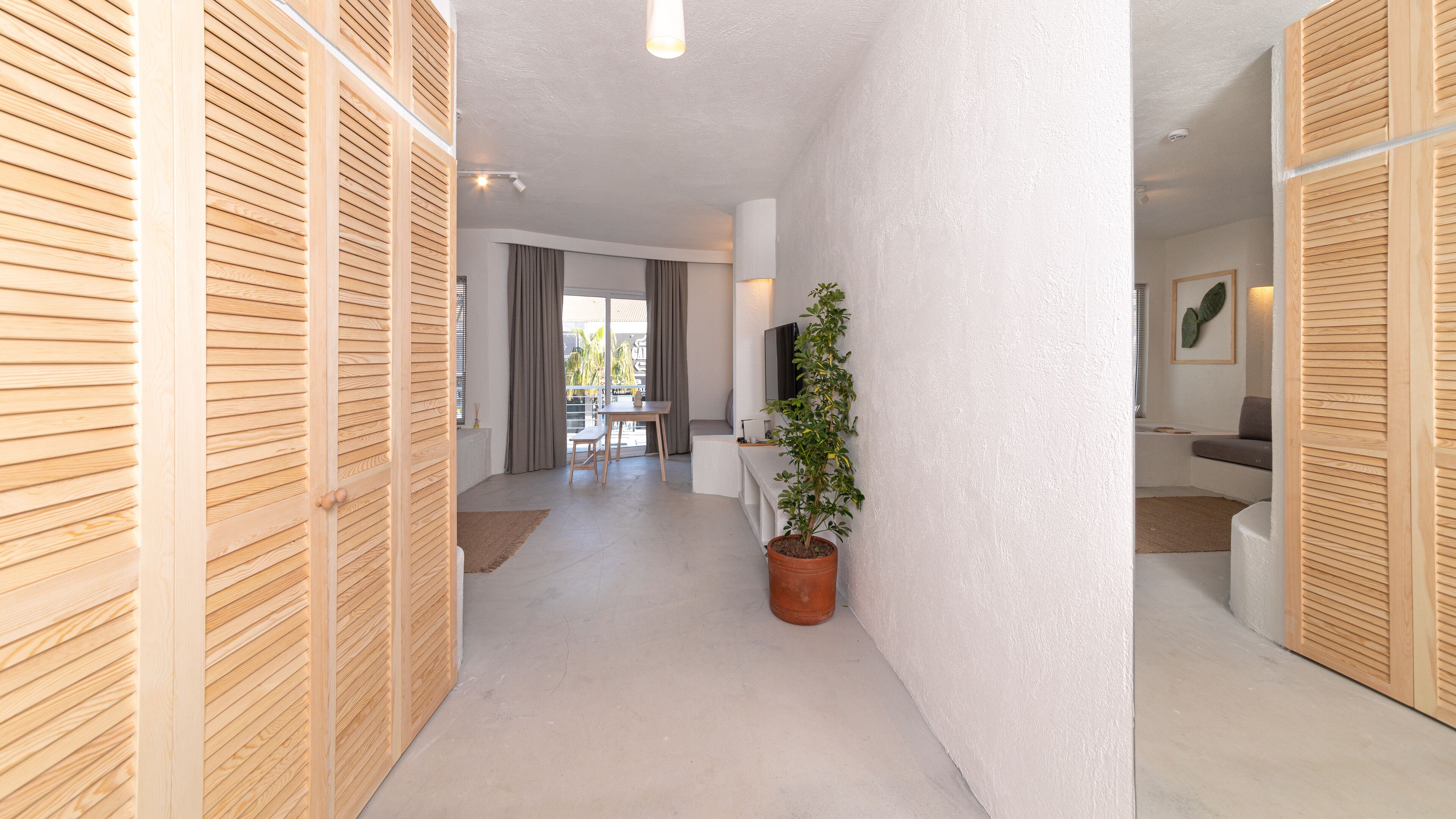 Un pasillo moderno con paneles de madera, una planta en maceta y un comedor con mesa y sillas.
