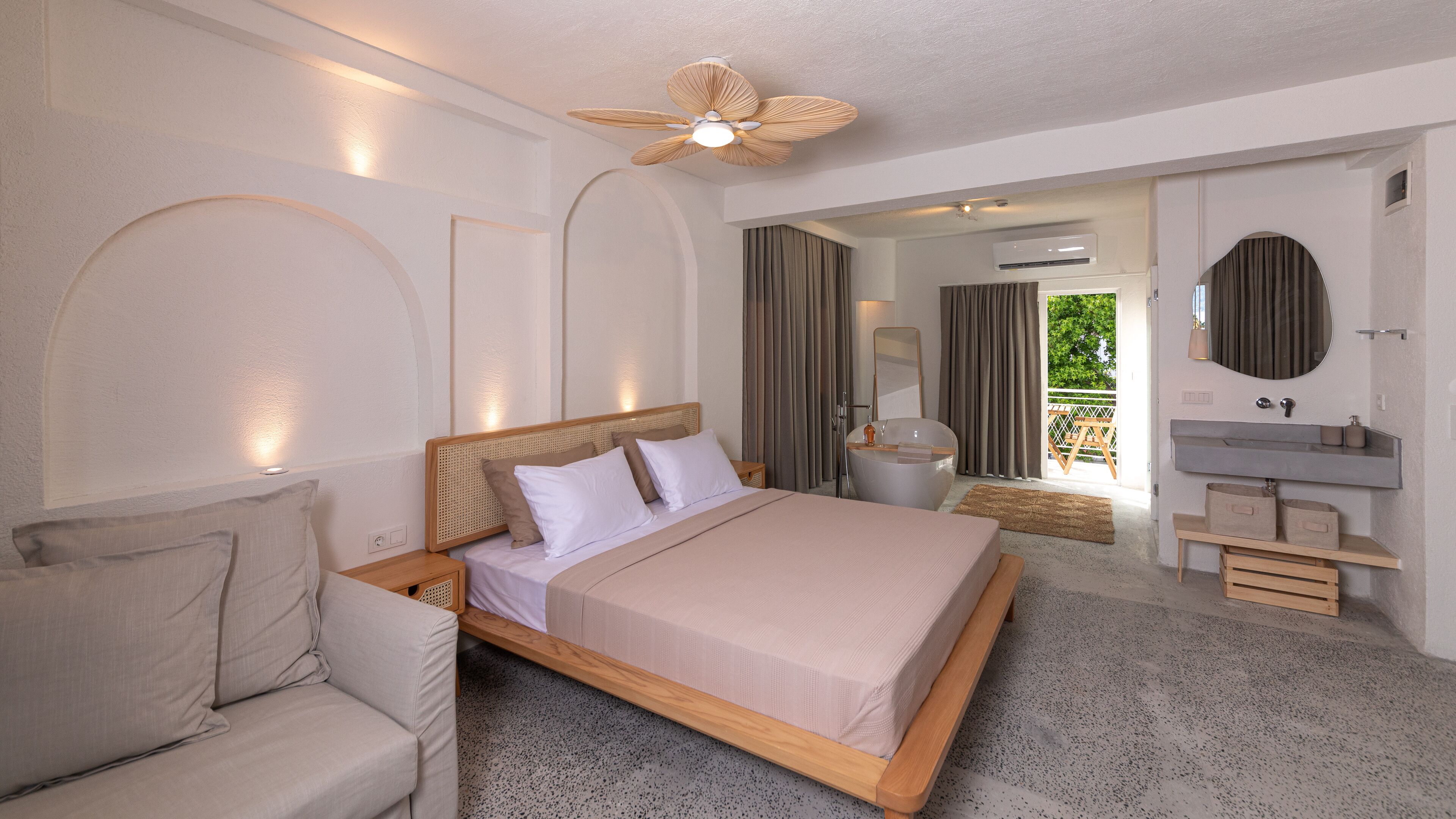 A modern bedroom with a large bed, a sofa, a vanity with a mirror, and a ceiling fan.