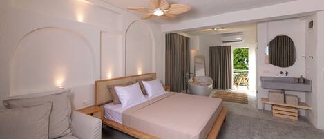 A modern bedroom with a large bed, a sofa, a vanity with a mirror, and a ceiling fan.