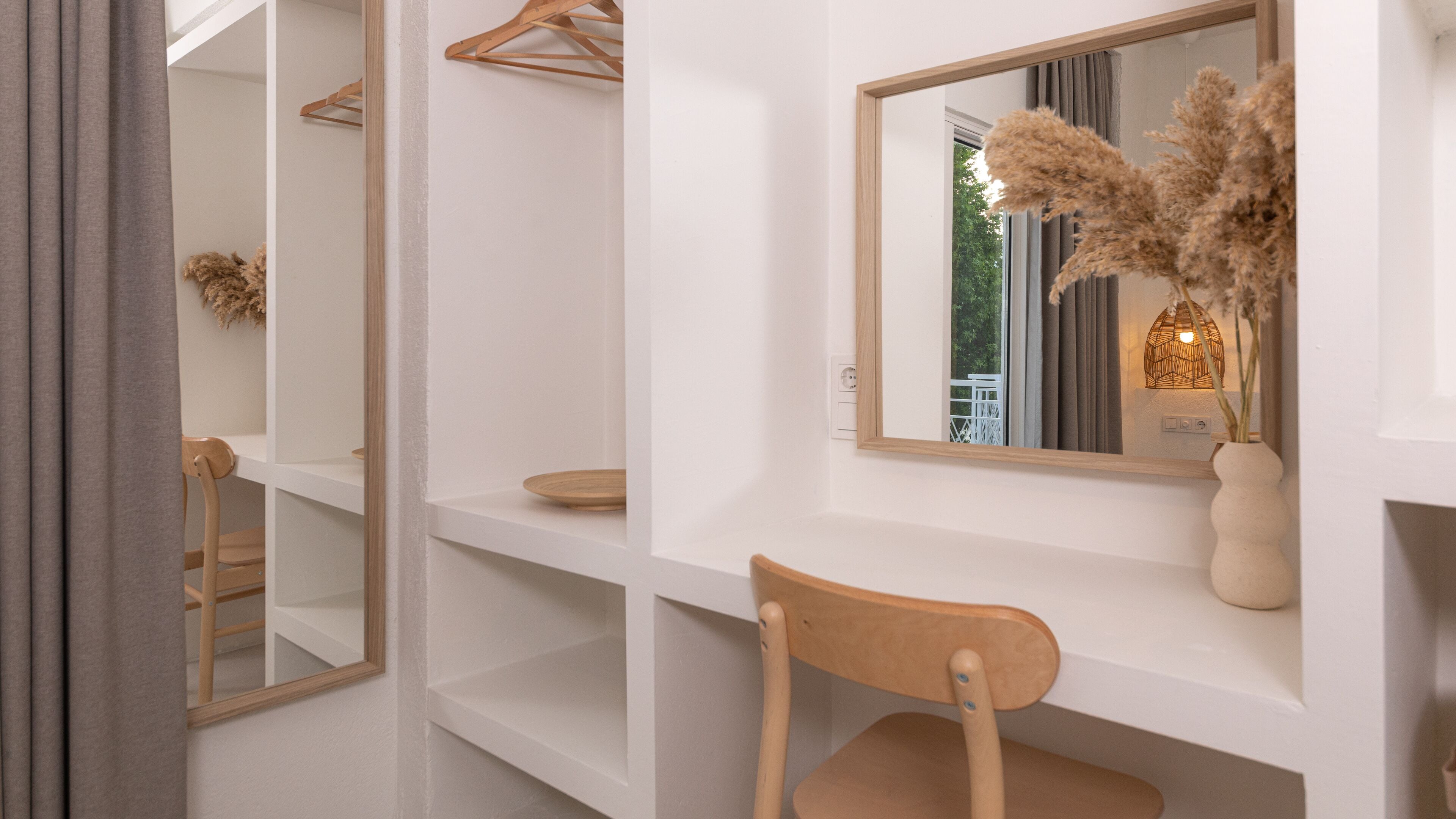 Een strakke badkamer met een houten stoel, een spiegel en een plank met een vaas gedroogde bloemen.