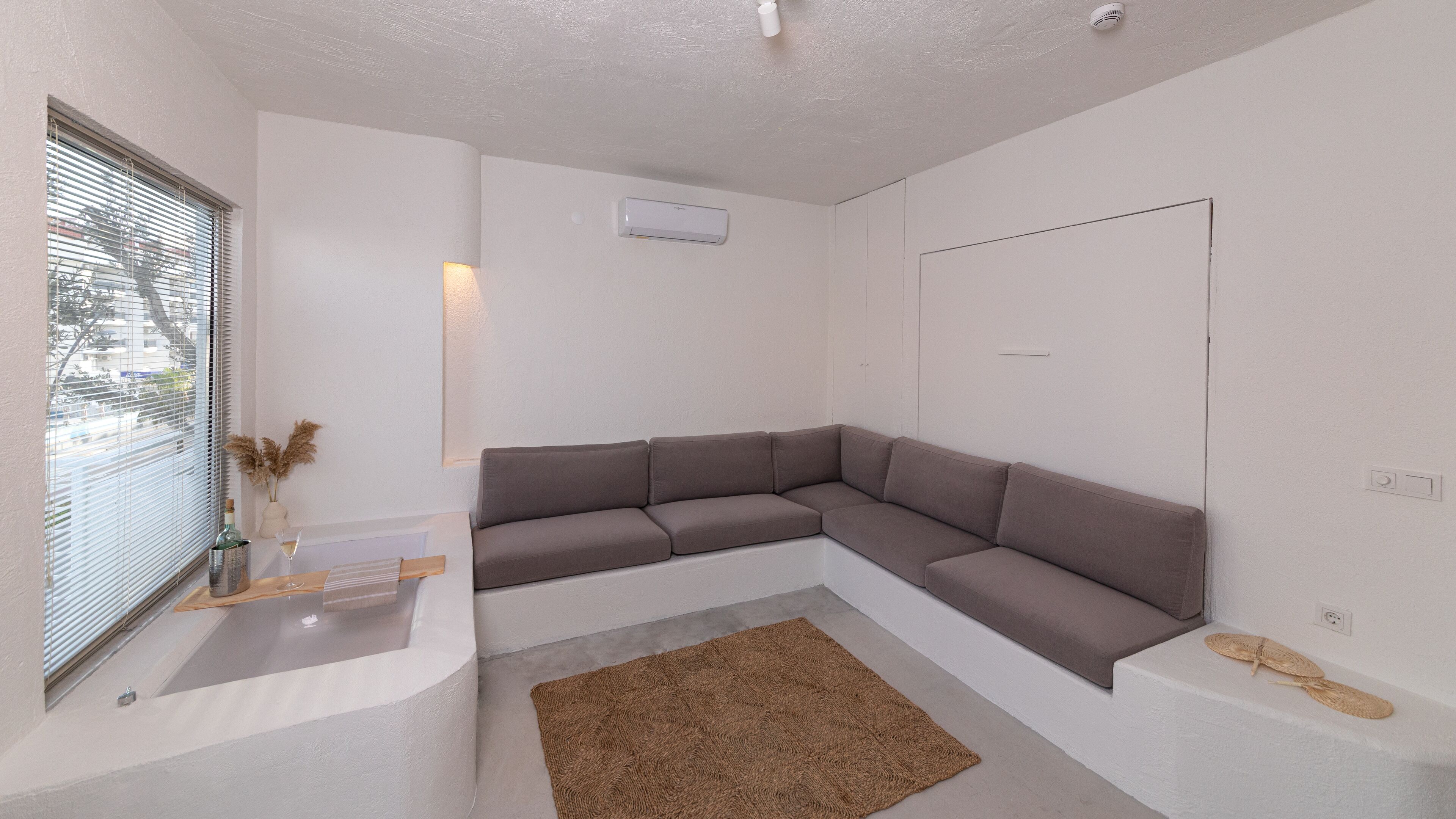 A modern living room with a sectional sofa, a small rug, and a window with blinds.