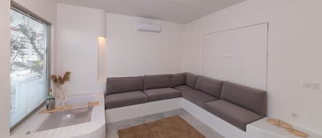 A modern living room with a sectional sofa, a small rug, and a window with blinds.