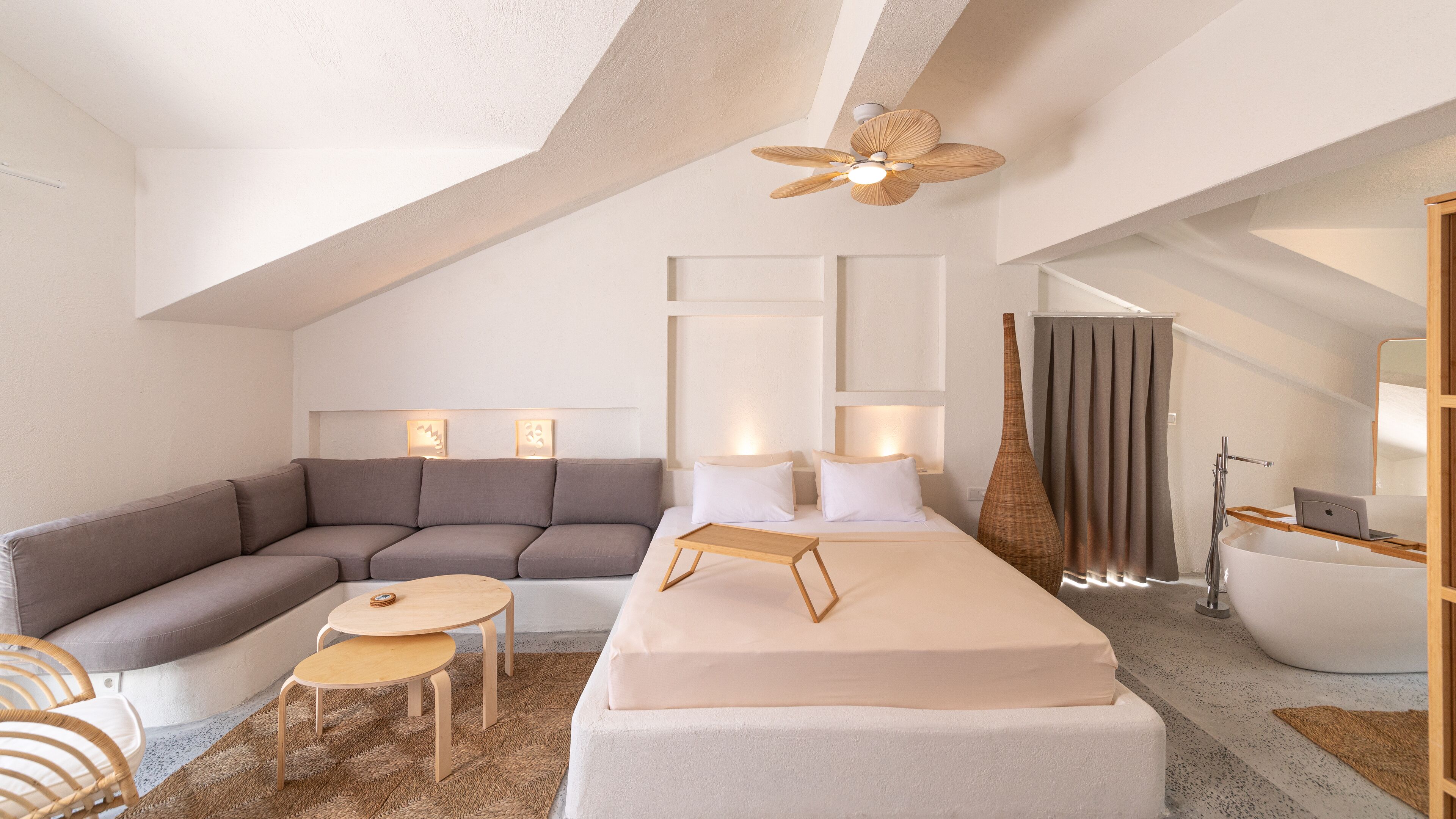 Een moderne, goed verlichte kamer met een groot bed, een bank, een kleine tafel en een plafondventilator.
