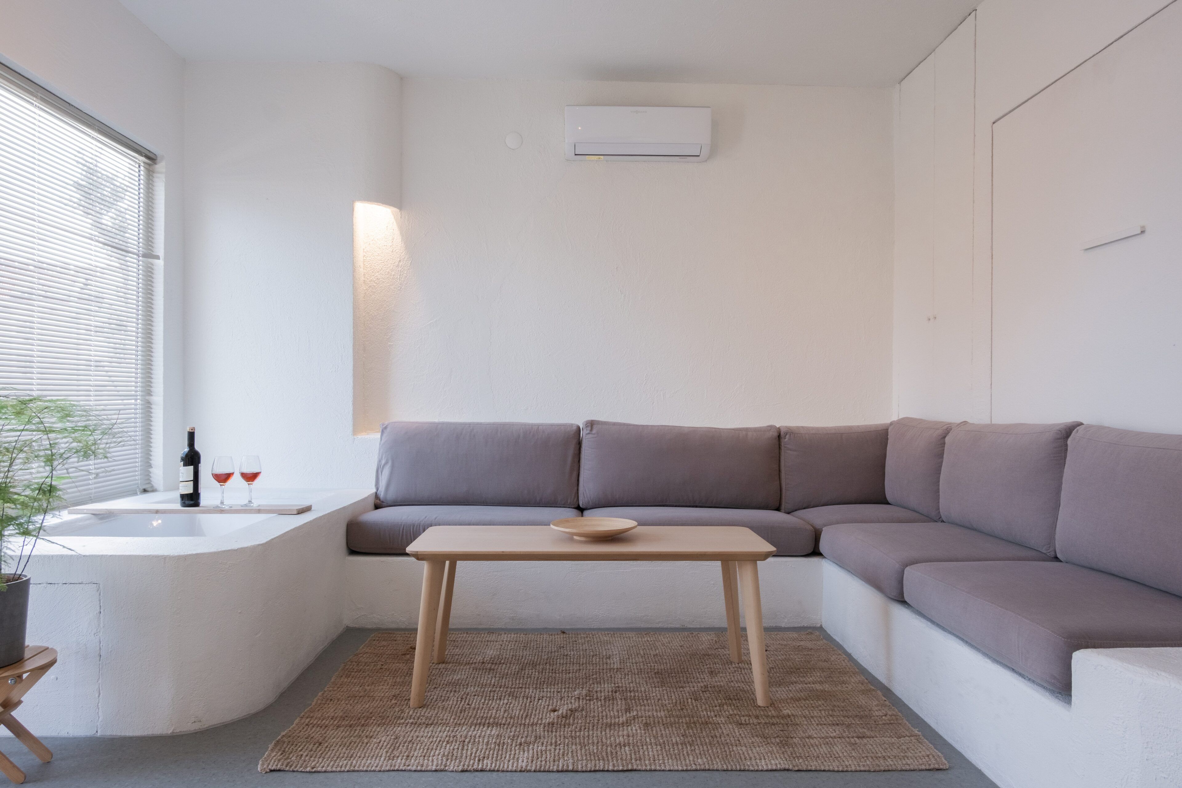 Un salon moderne avec un canapé d’angle gris, une table basse en bois et une petite table d’appoint sur laquelle se trouvent une bouteille et des verres.