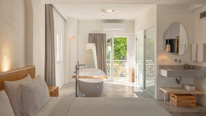 Una habitación de hotel moderna con una cama grande, una bañera, un balcón con vistas y un baño con lavabo y espejo.