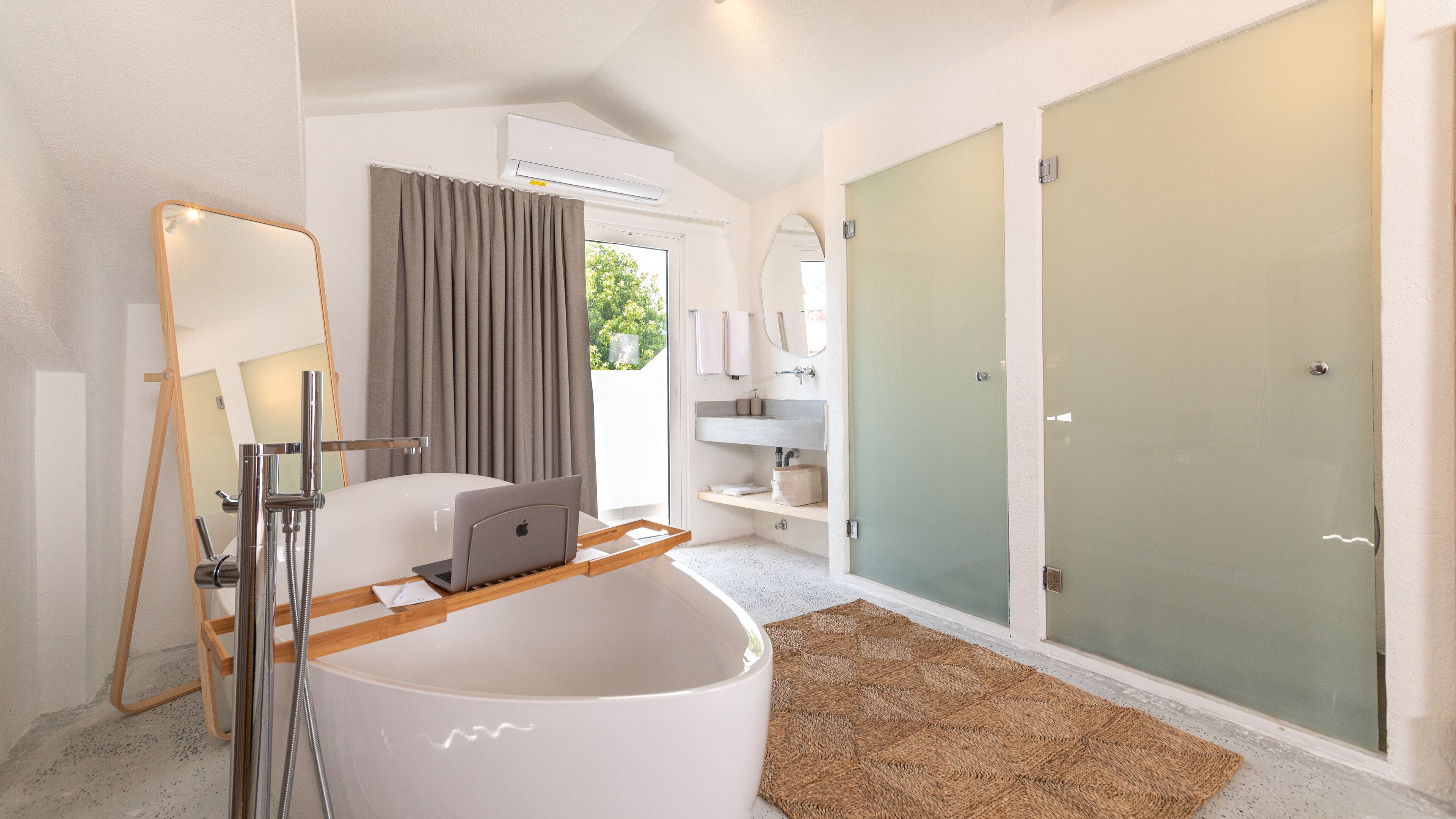 Une salle de bain moderne avec une baignoire, une douche et des toilettes. On y trouve une chaise en bois et un ordinateur portable posés sur le sol.