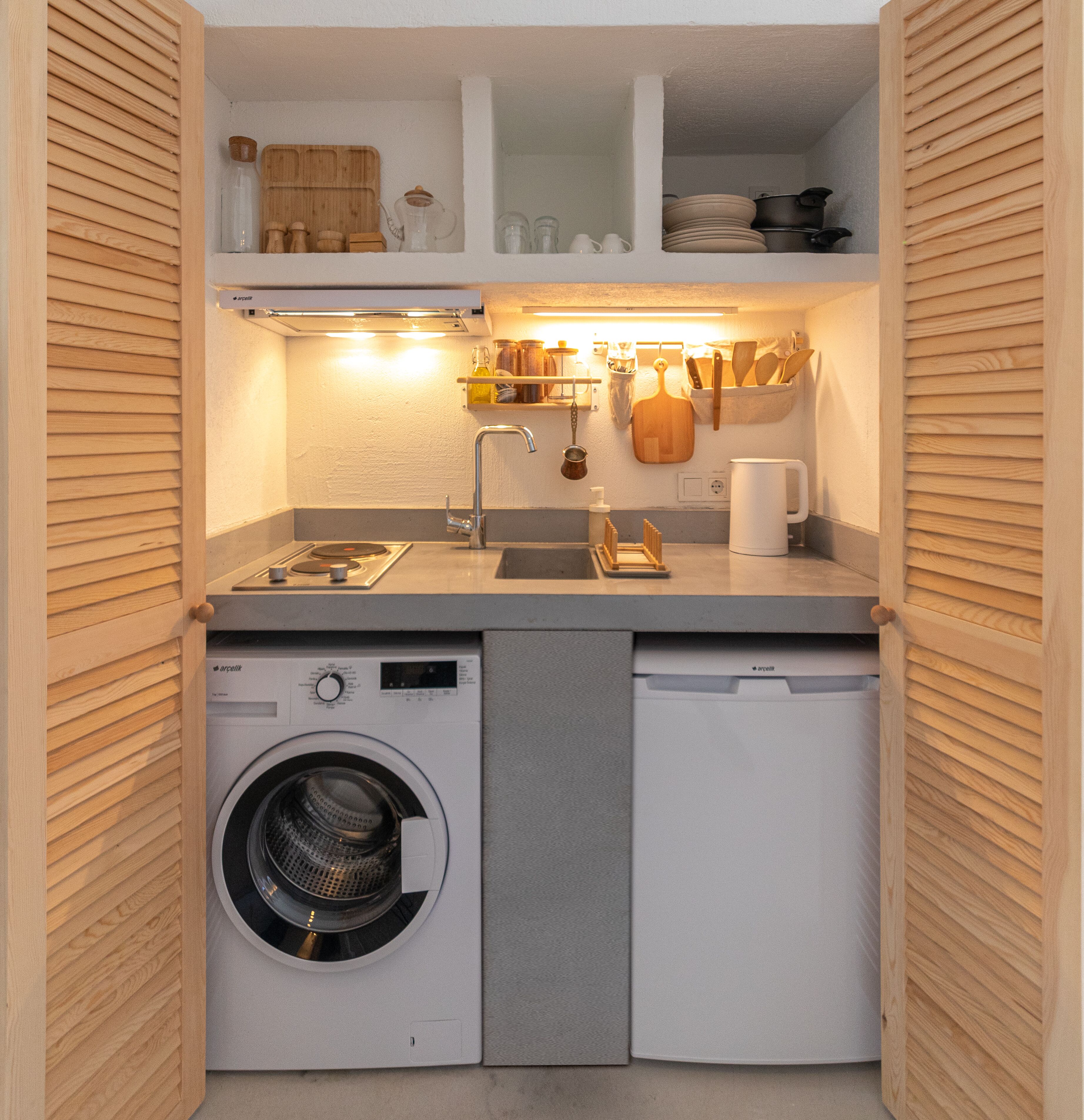 A compact kitchen with a built-in washing machine, a sink, and a countertop with various kitchen utensils and appliances.