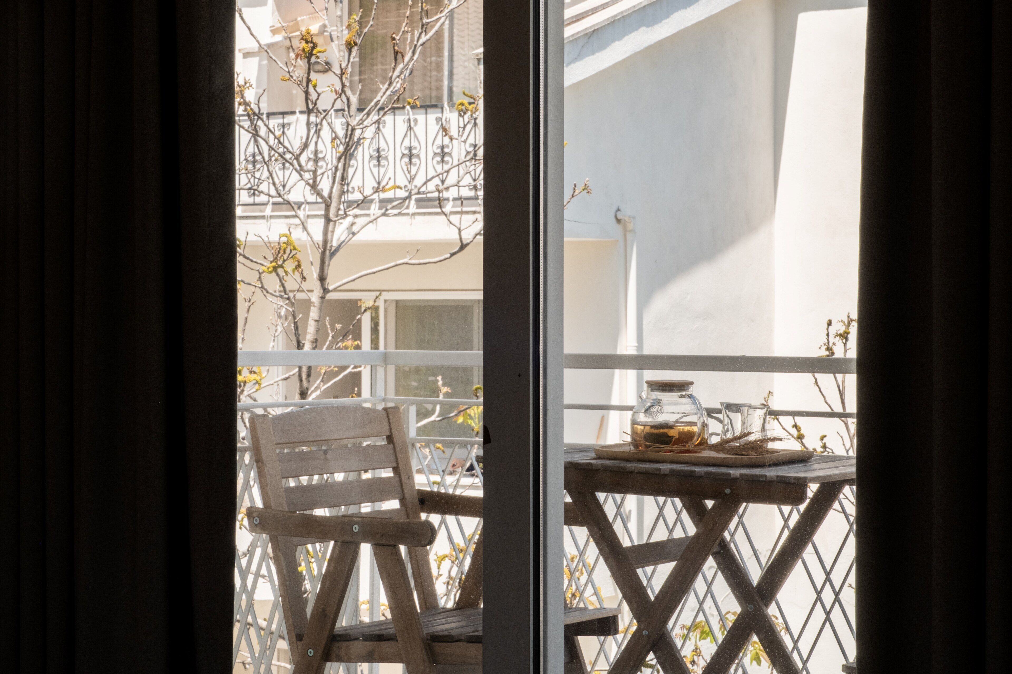 Un balcón con una silla de madera y una mesa con una jarrón de vidrio y un plato.
