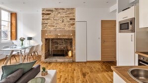 A modern kitchen with a stone fireplace, wooden beams, and a dining area with a table and chairs. - Le Cerf Volant - une pépite à l'Intramuros (Saint-Malo)