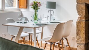 A dining area with a round table, white chairs, a vase with flowers, and a lamp. - Le Cerf Volant - une pépite à l'Intramuros (Saint-Malo)