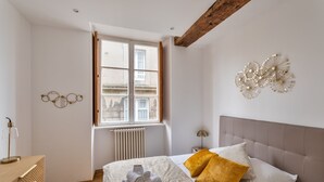 A bedroom with a bed, a window, a radiator, a wooden floor, and a wall with a decorative piece. - Le Cerf Volant - une pépite à l'Intramuros (Saint-Malo)