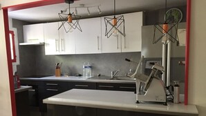 A modern kitchen with white cabinets, a central island, and pendant lighting. - Appartement Rez de Jardin Piscine Chauffée, Barbecue, Plancha (Argelès-sur-Mer)
