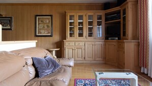 A living room with a beige sofa, a glass coffee table, wooden cabinets, and a television.