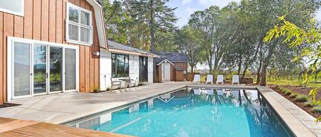 A modern house with a swimming pool, wooden deck, and a view of trees.