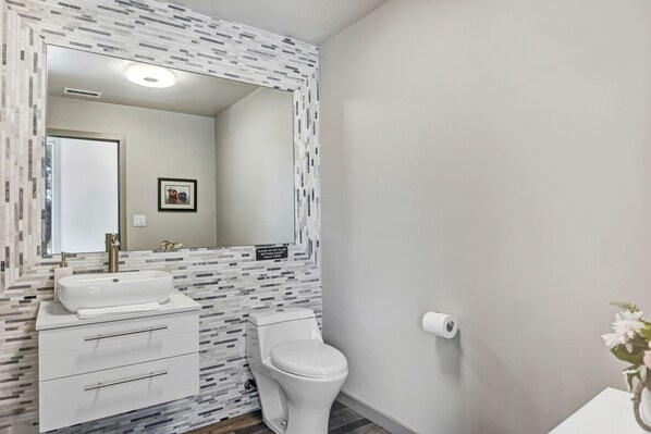 Un baño con lavamanos, espejo y retrete blancos.
