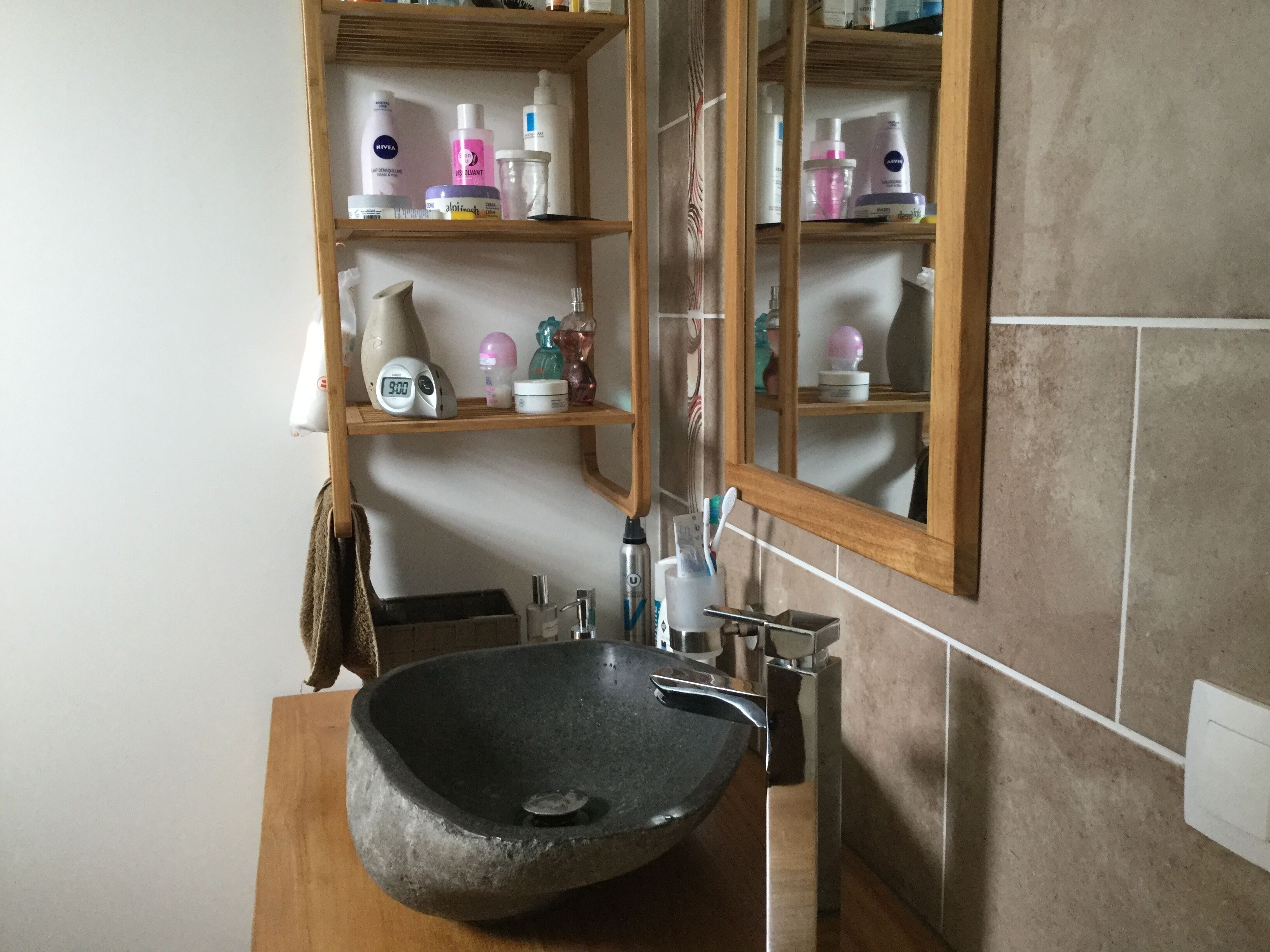 Une salle de bain avec un lavabo en pierre, des étagères contenant des articles de toilette, un miroir et un porte-serviettes.